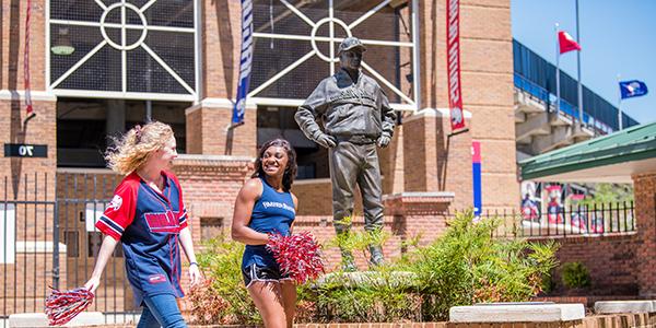 Two students walking outside of the stadium holding pom poms.